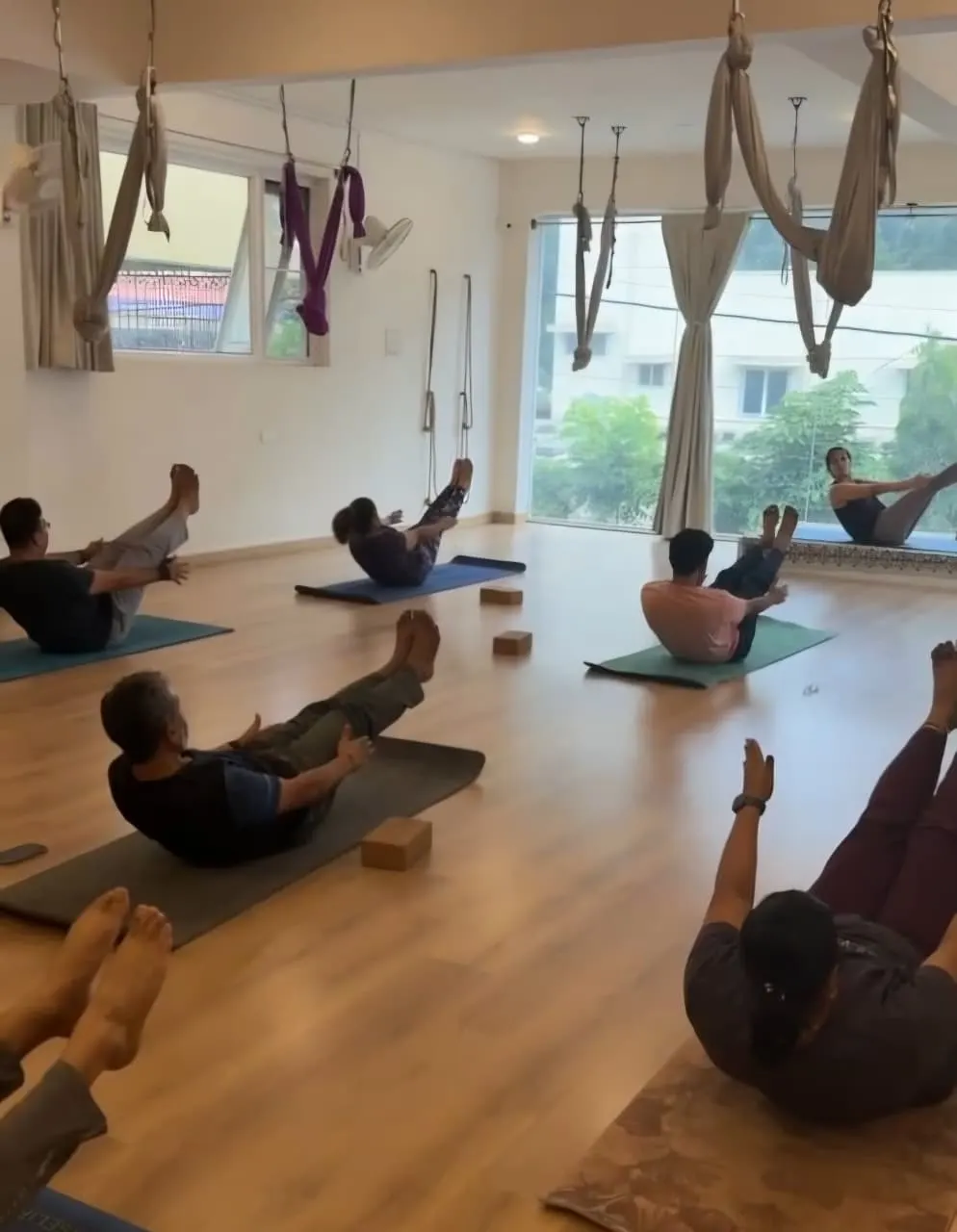 Anusha leading an in-person class as students hold boat pose on mats in a bright studio